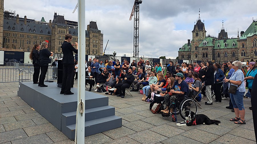 A crowd on Parliament Hill watches speakers sign from a podium at the Deaf Flag Day ceremony
